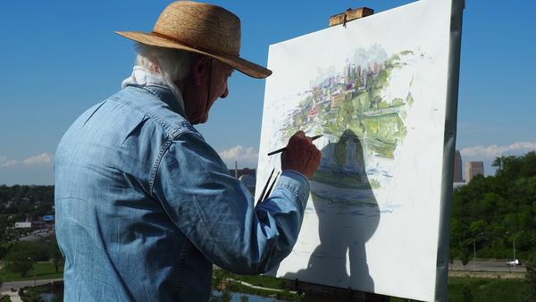 A daylight photo of a man painting on a white paper