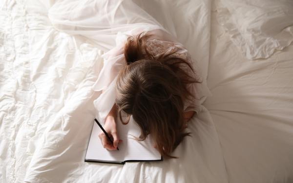 A lady wrapped in a white cloth writing on book on a bed