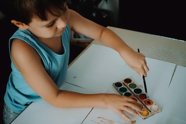 A photo of a boy using a water color to paint on a white paper