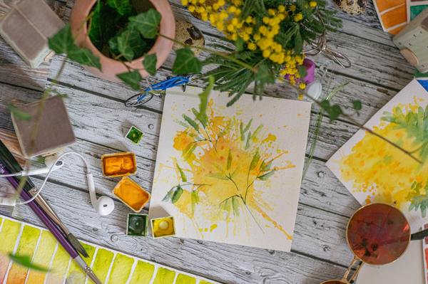 A photo of a yellow painting on a white paper with earpiece at the side and paint brushes