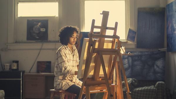 A photo of lady in an art studio painting on an easel